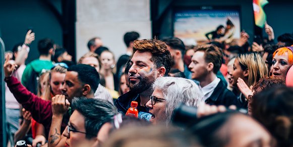 A crowd of people at a march. A man and a woman are in the centre. The man has coloured face paint on his cheek and the woman has grey hair and black glasses.